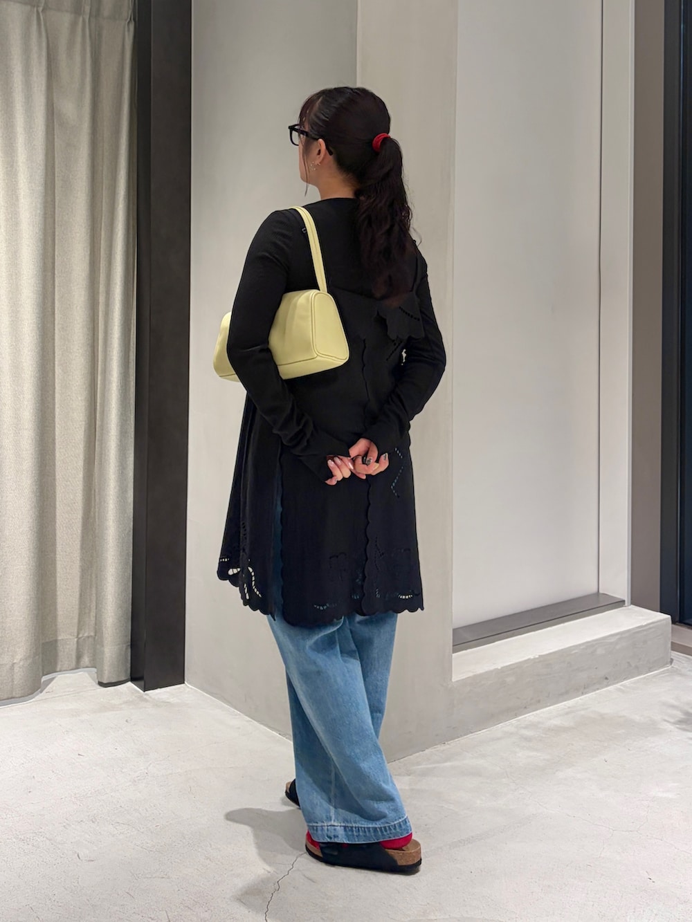 ブルー系のデニムパンツ、ブラック系のカーディガン/ボレロ、イエロー系のハンドバッグを着用したレディースの夏コーディネートの3枚目の写真