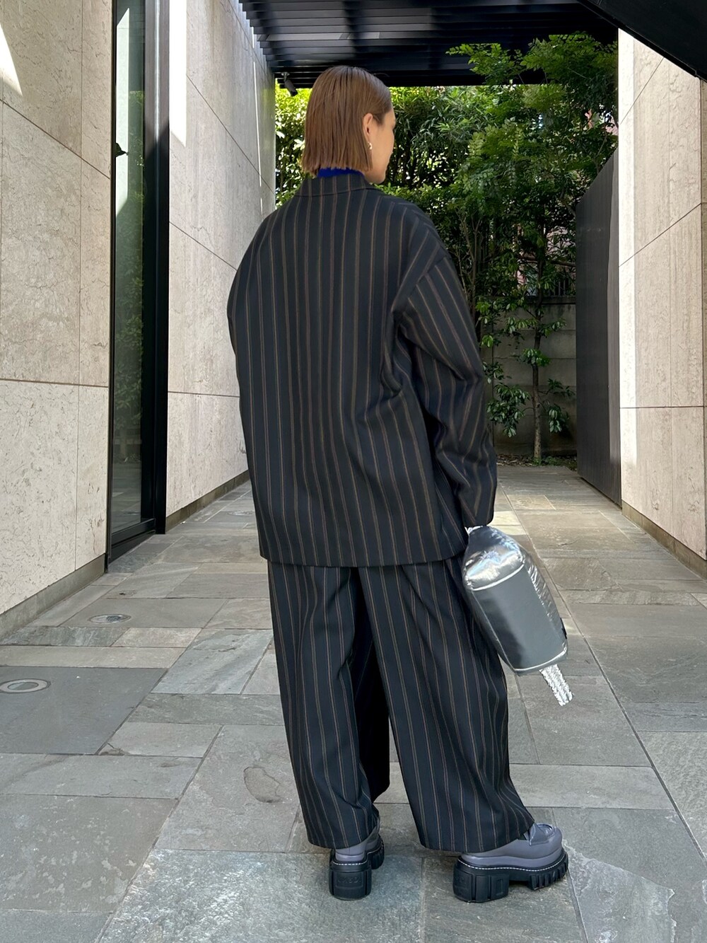 ブラック系のテーラードジャケット、ブラック系のスラックス、シルバー系のハンドバッグを着用したレディースの夏コーディネートの2枚目の写真