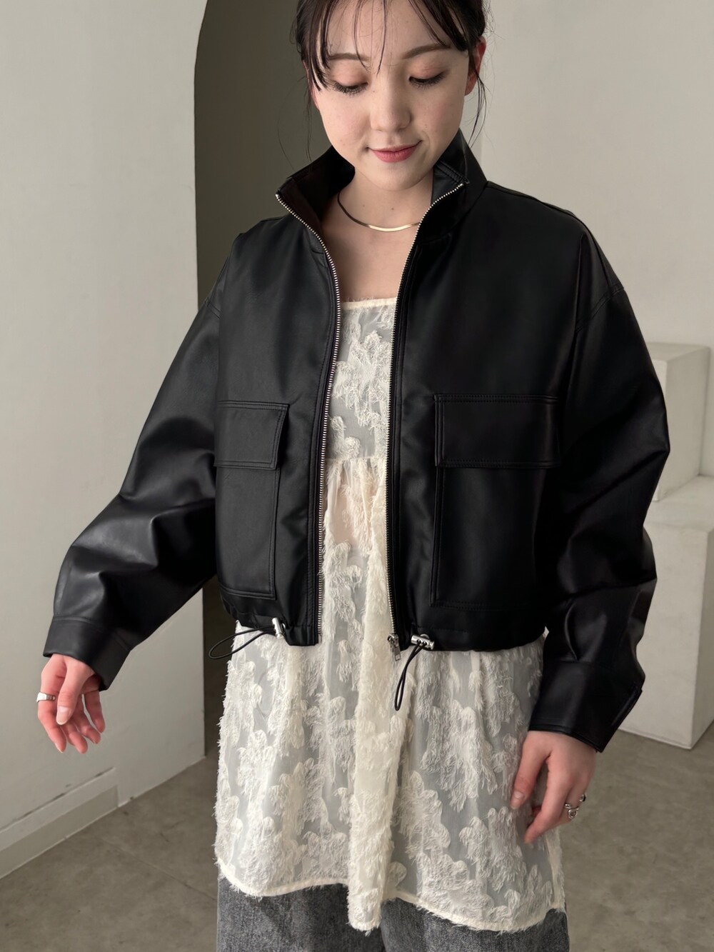 ホワイト系のチュニック、ブラック系のブルゾン、グレー系のデニムパンツを着用したレディースの春コーディネートの6枚目の写真