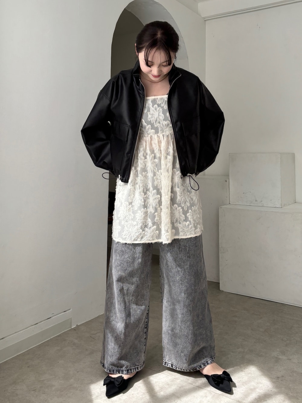 ホワイト系のチュニック、ブラック系のブルゾン、グレー系のデニムパンツを着用したレディースの春コーディネートの4枚目の写真