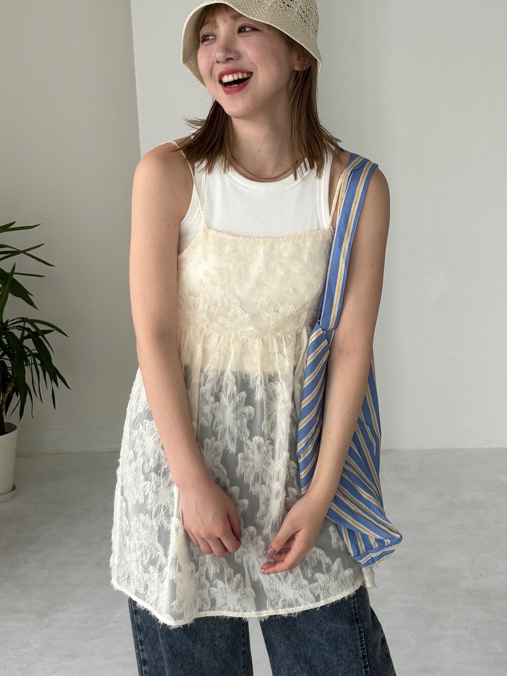 ブルー系のトートバッグ、ホワイト系のチュニック、ブルー系のデニムパンツを着用したレディースの夏コーディネートの5枚目の写真