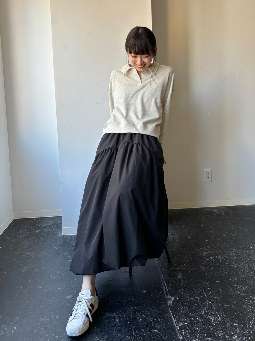 ブラック系のスカート、ホワイト系のスニーカー、ベージュ系のポロシャツを着用したレディースの冬コーディネートの2枚目の写真