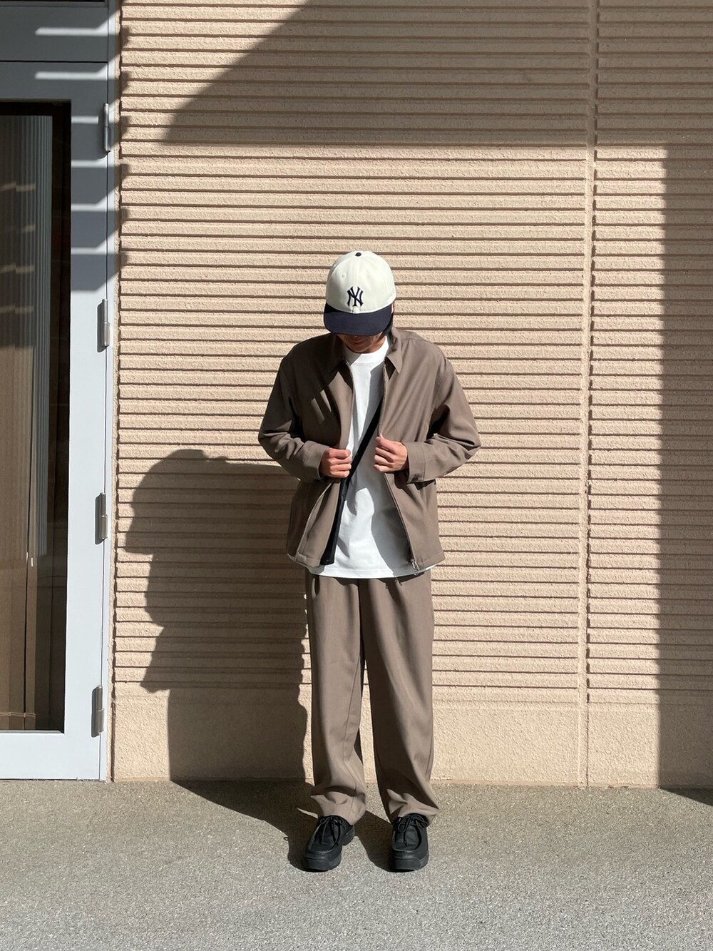 ブラウン系のブルゾン、ブラック系のショルダーバッグ、ホワイト系のTシャツ/カットソーを着用したメンズの春コーディネートの2枚目の写真