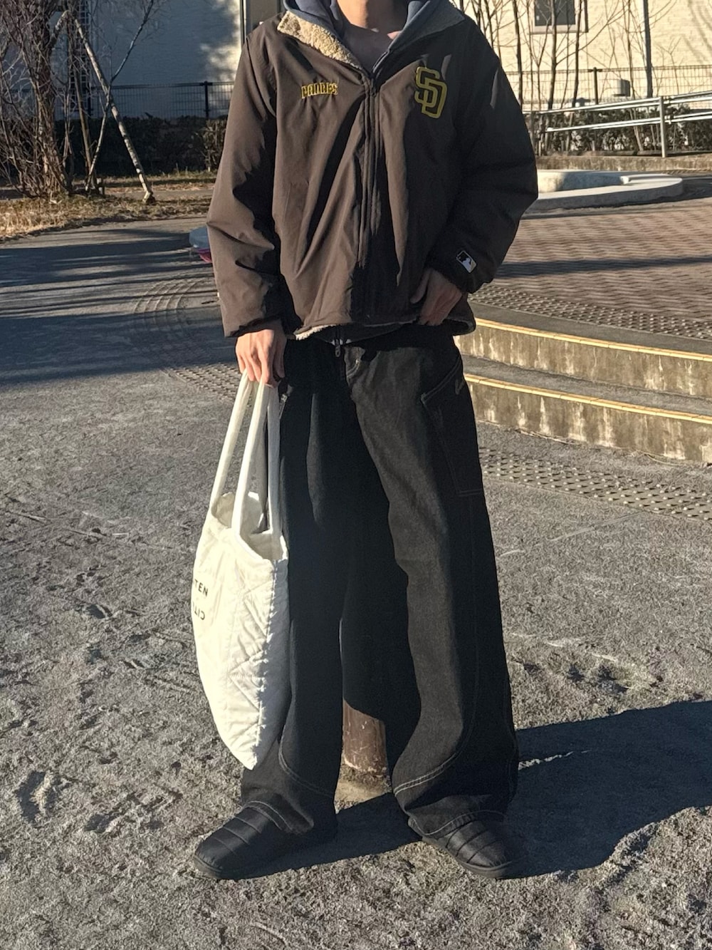 ブラウン系のブルゾン、ホワイト系のトートバッグを着用したメンズの冬コーディネートの2枚目の写真