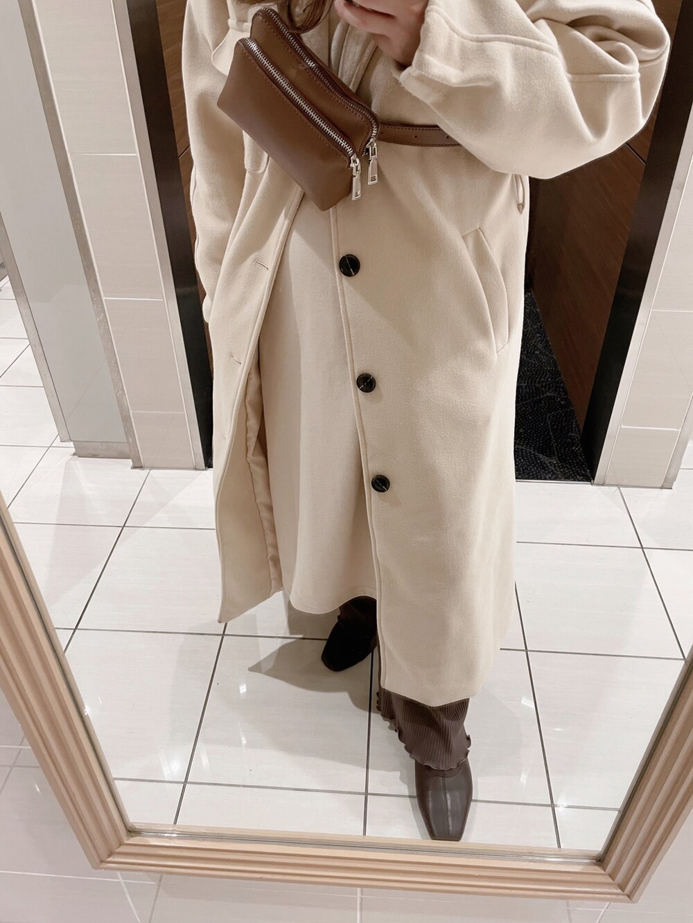 ホワイト系のステンカラーコート、ブラウン系のショルダーバッグ、ベージュ系のワンピースを着用したレディースの冬コーディネートの2枚目の写真