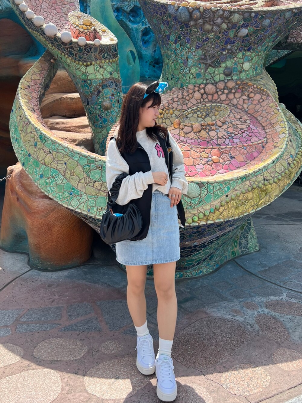 ブラック系のベスト、ブルー系のデニムスカート、ホワイト系のスニーカーを着用したレディースの春コーディネートの2枚目の写真