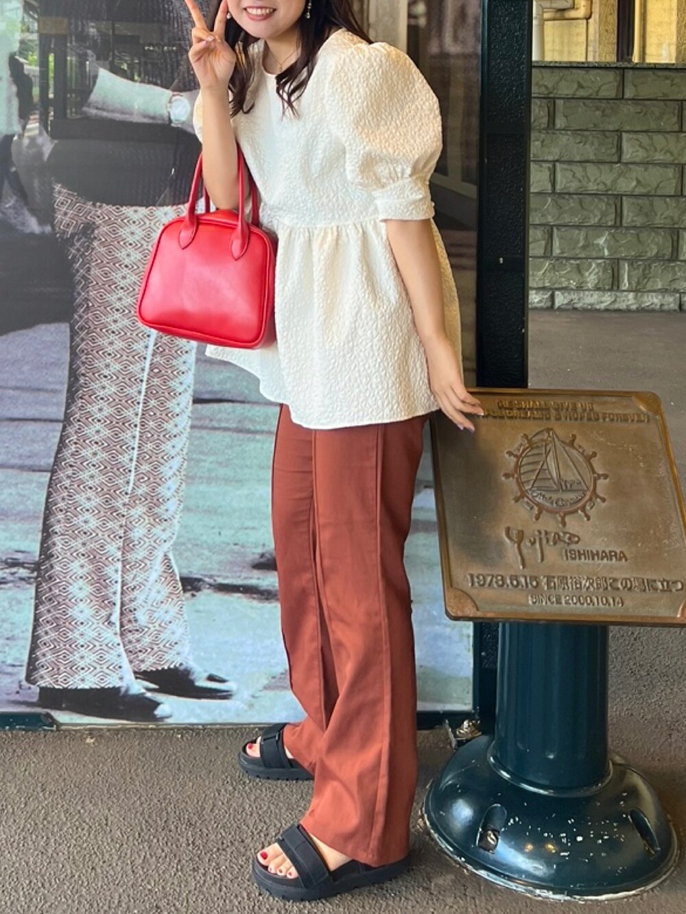 レッド系のボストンバッグ、ホワイト系のシャツ/ブラウス、オレンジ系のスラックスを着用したレディースの夏コーディネートの2枚目の写真