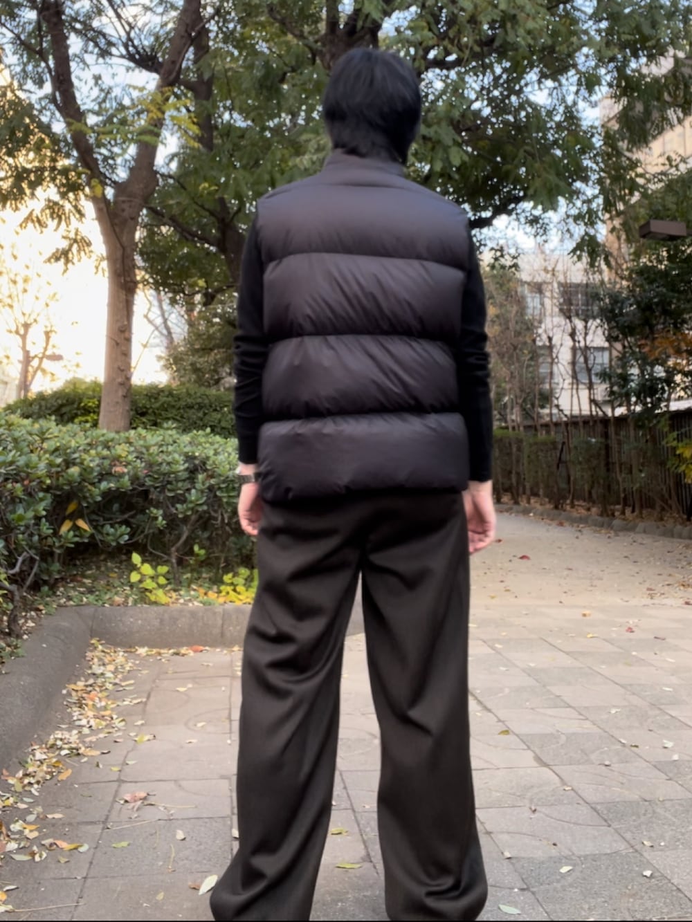 ブラウン系のスラックス、ブラック系のダウンベスト、ブラック系のTシャツ/カットソーを着用したメンズの冬コーディネートの3枚目の写真