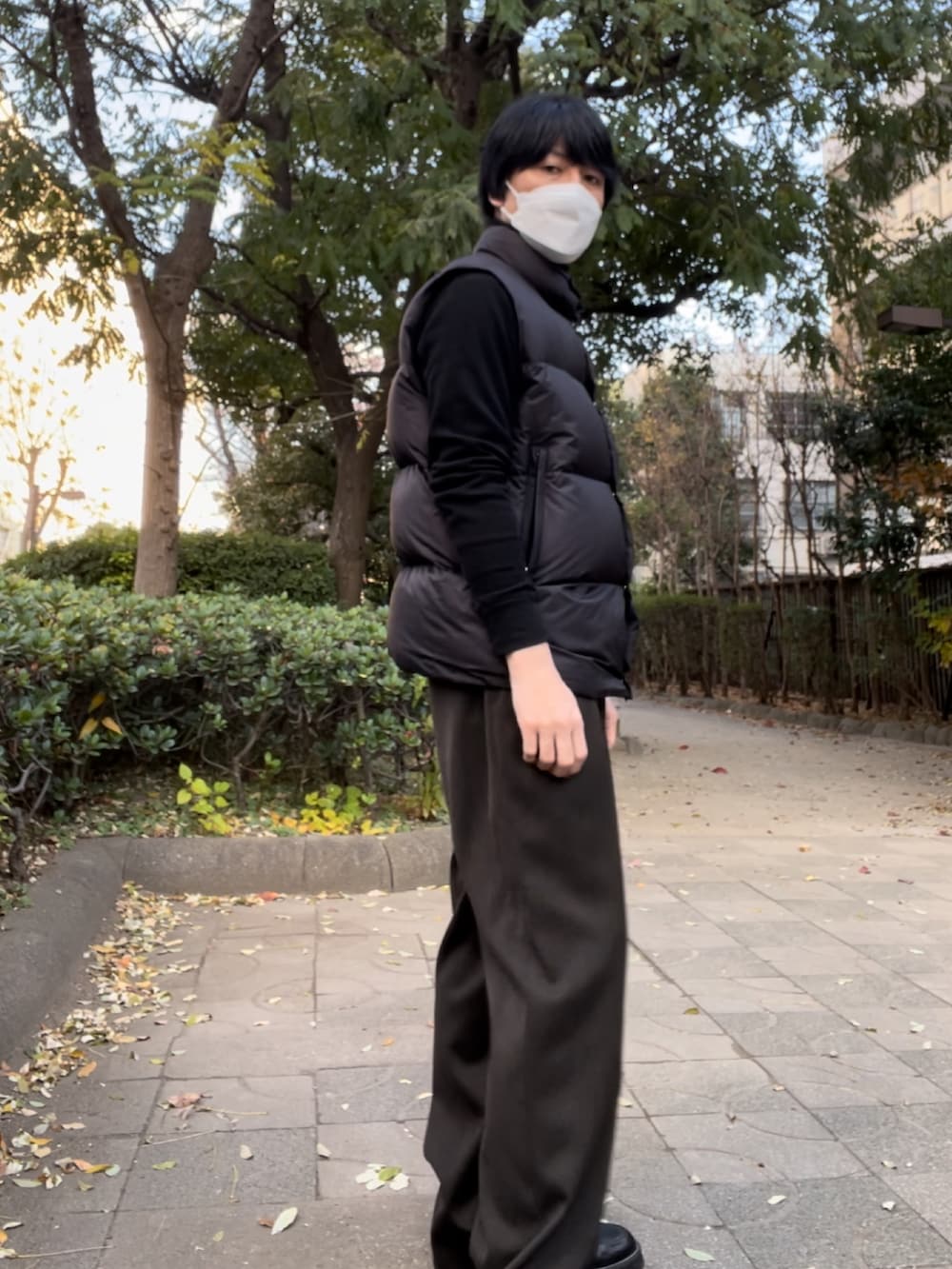 ブラウン系のスラックス、ブラック系のダウンベスト、ブラック系のTシャツ/カットソーを着用したメンズの冬コーディネートの2枚目の写真