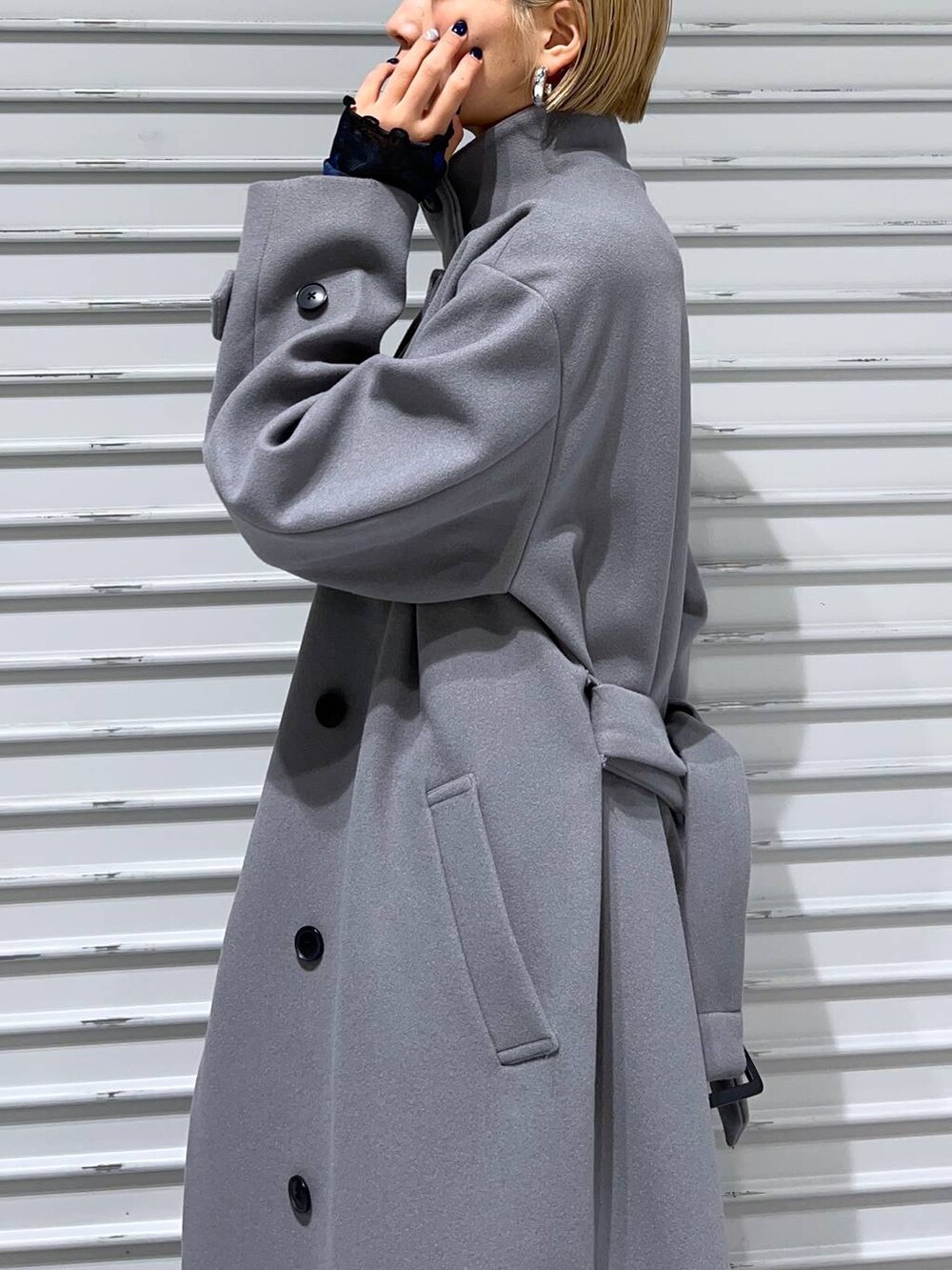 グレー系のチェスターコート、ブラック系のブーツ、ブルー系のスカートを着用したレディースの秋コーディネートの2枚目の写真