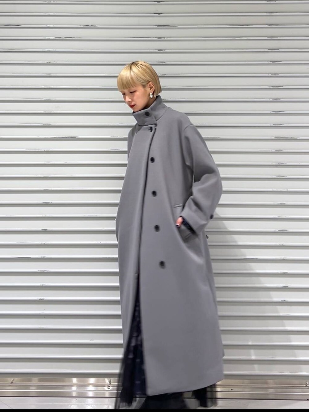 グレー系のチェスターコート、ブラック系のブーツ、ブルー系のスカートを着用したレディースの秋コーディネートの7枚目の写真