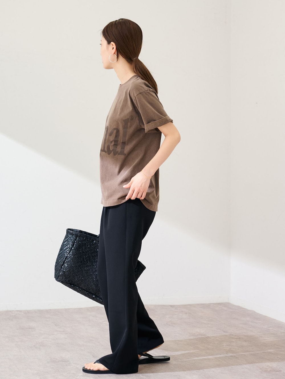 ブラック系のスラックス、ブラウン系のTシャツ/カットソー、ブラック系のトートバッグを着用したレディースの春コーディネートの2枚目の写真