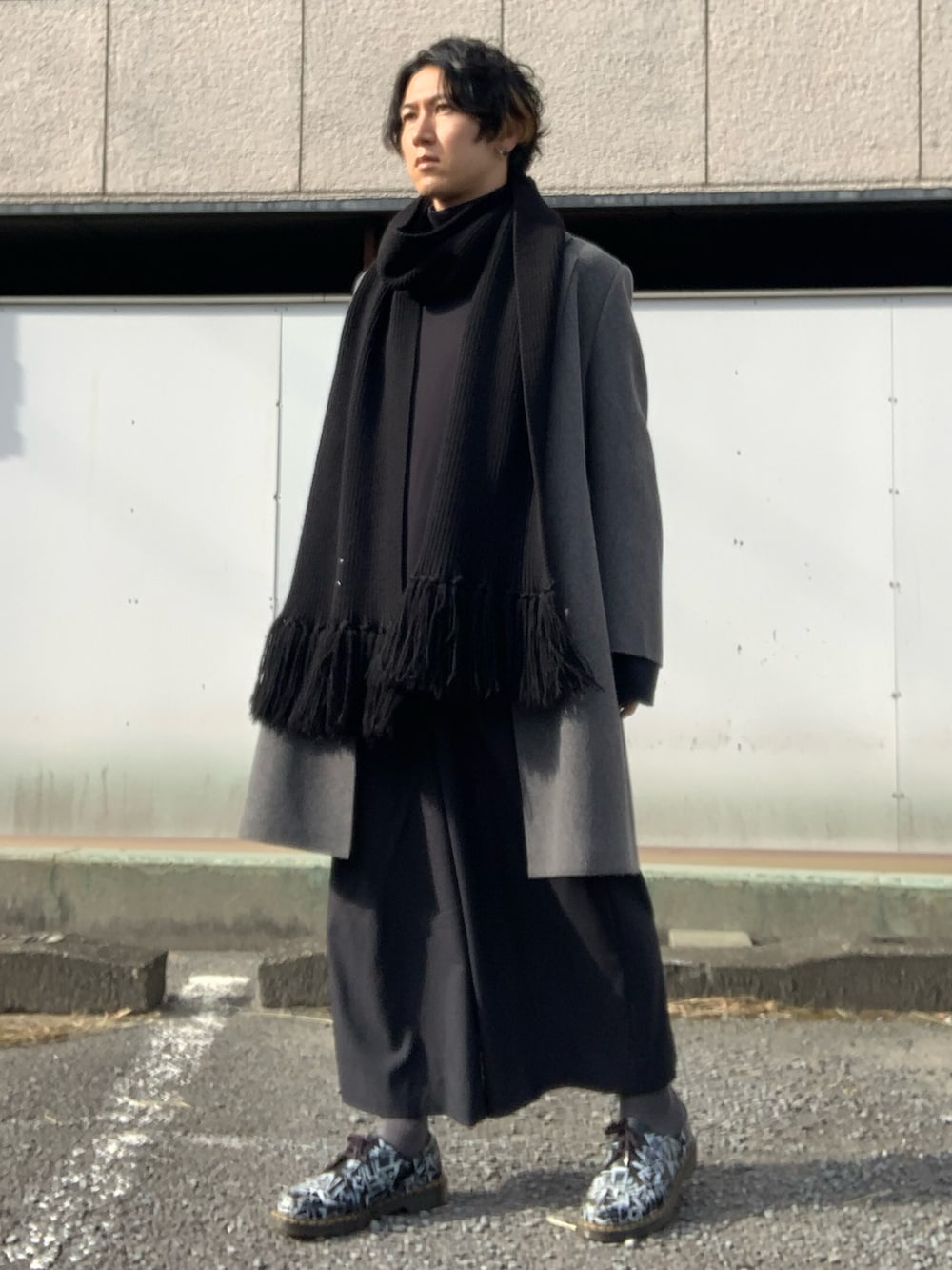 グレー系のチェスターコート、ブラック系のTシャツ/カットソー、ブラック系のスラックスを着用したメンズの冬コーディネートの3枚目の写真