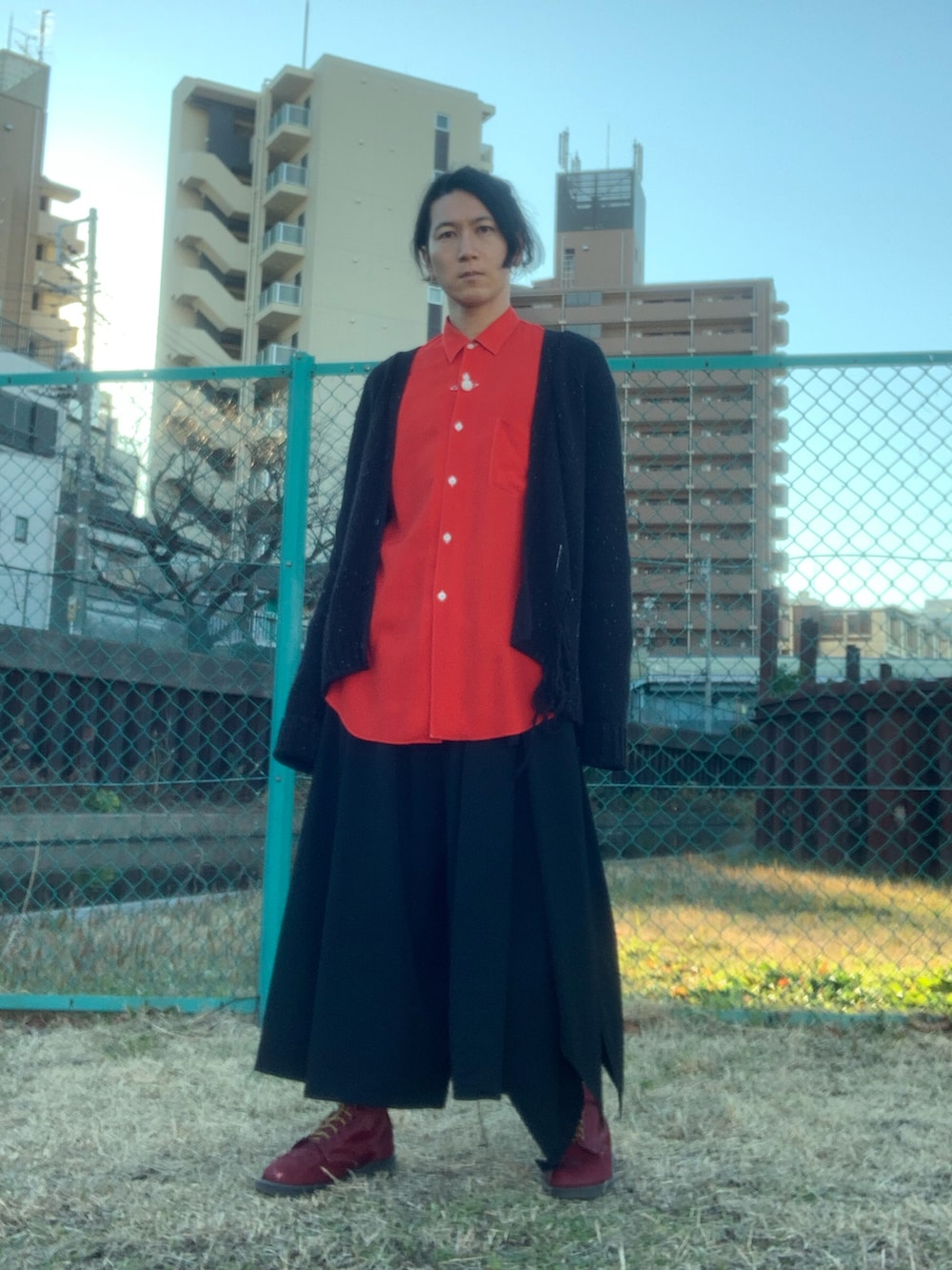 レッド系のブーツ、ブラック系のスラックス、ブラック系のカーディガン/ボレロを着用したメンズの冬コーディネートの2枚目の写真