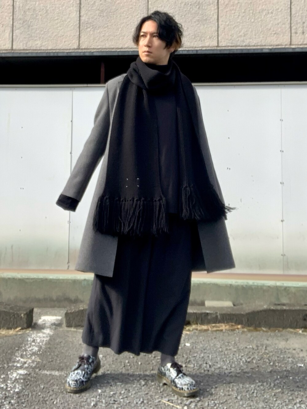 グレー系のチェスターコート、ブラック系のTシャツ/カットソー、ブラック系のスラックスを着用したメンズの冬コーディネートの2枚目の写真