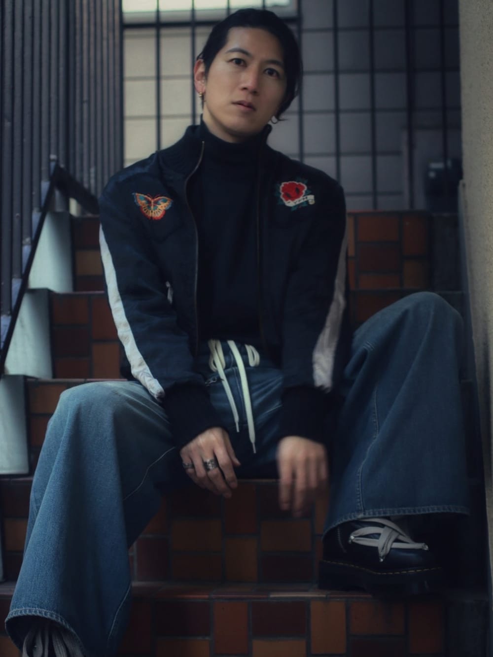 ブルー系のデニムパンツ、ブラック系のTシャツ/カットソー、ブラック系のスカジャンを着用したメンズの春コーディネートの4枚目の写真