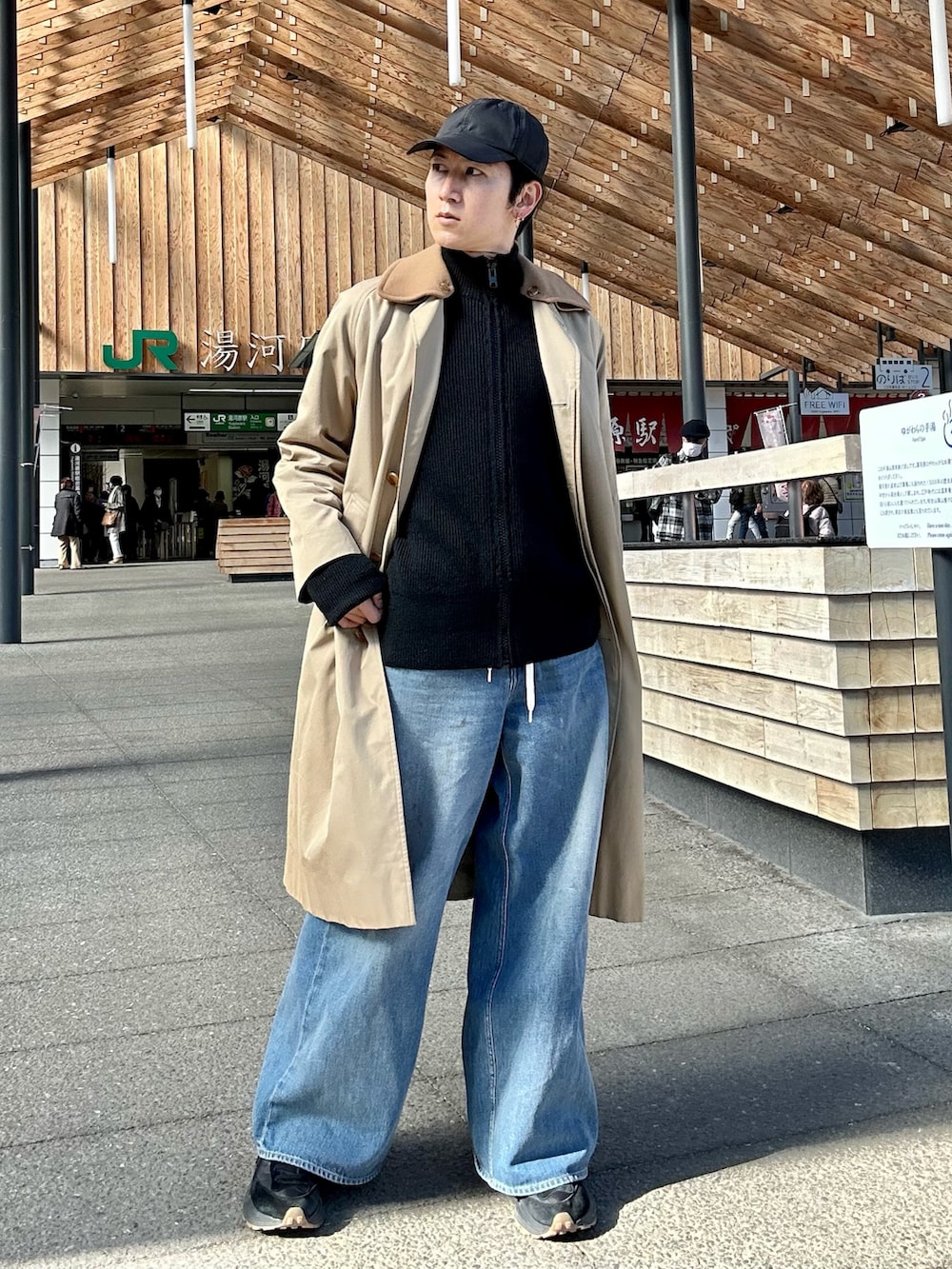 ブラック系のニット/セーター、ベージュ系のステンカラーコート、ブルー系のデニムパンツを着用したメンズの冬コーディネートの2枚目の写真