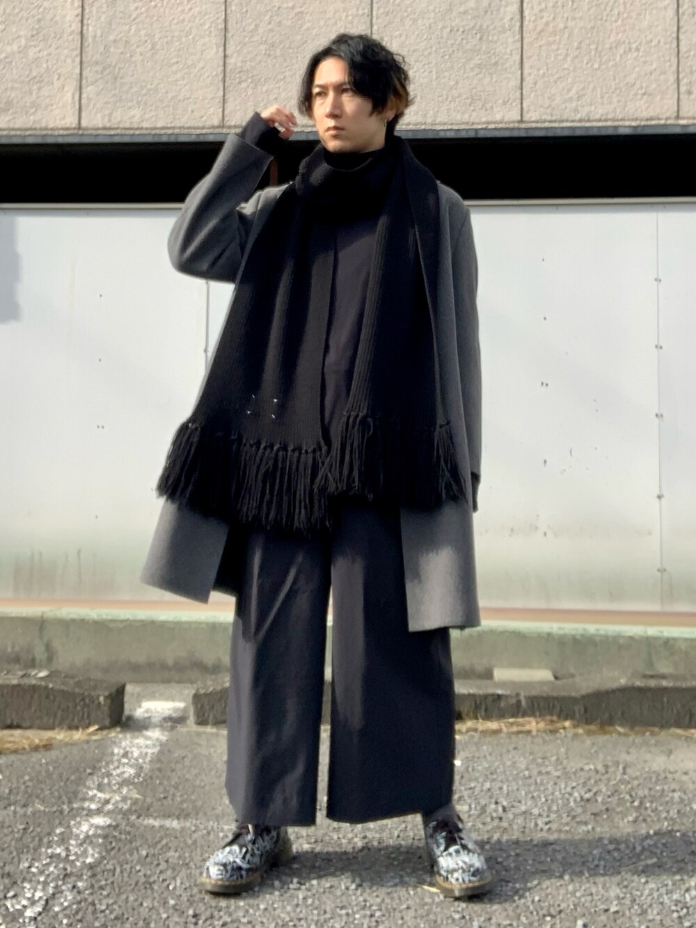 グレー系のチェスターコート、ブラック系のTシャツ/カットソー、ブラック系のスラックスを着用したメンズの冬コーディネートの5枚目の写真