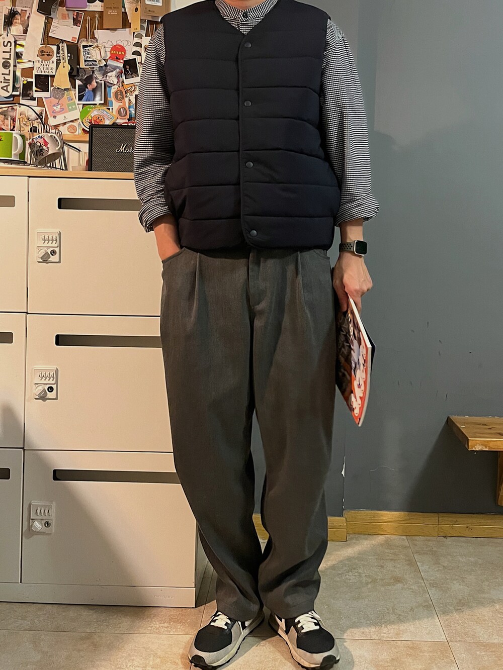ブラック系のスニーカー、グレー系のスラックス、ブラック系のダウンベストを着用したメンズの春コーディネートの2枚目の写真