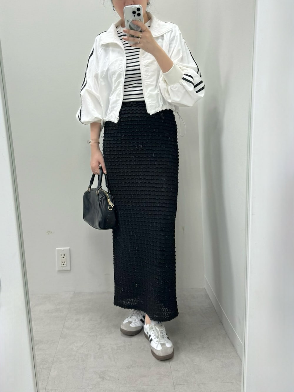 ブラック系のボストンバッグ、ホワイト系のナイロンジャケット、ホワイト系のスカートを着用したレディースの春コーディネートの2枚目の写真