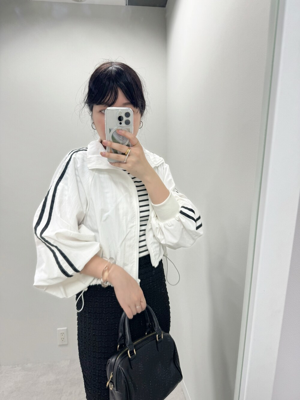 ブラック系のボストンバッグ、ホワイト系のナイロンジャケット、ホワイト系のスカートを着用したレディースの春コーディネートの3枚目の写真