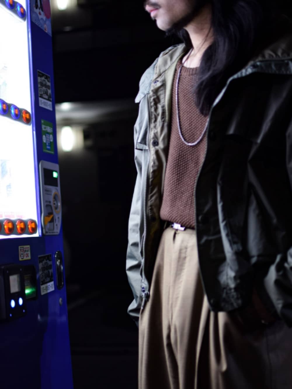 グリーン系のナイロンジャケット、ブラウン系のニット/セーター、ベージュ系のスラックスを着用したメンズの春コーディネートの2枚目の写真