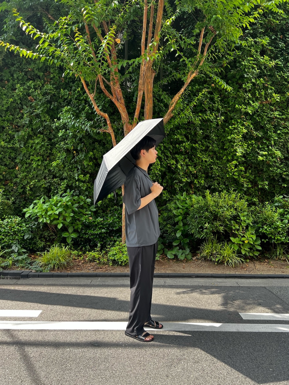 グレー系のTシャツ/カットソー、ブラック系のその他パンツ、ブラック系の折りたたみ傘を着用したメンズの夏コーディネートの2枚目の写真