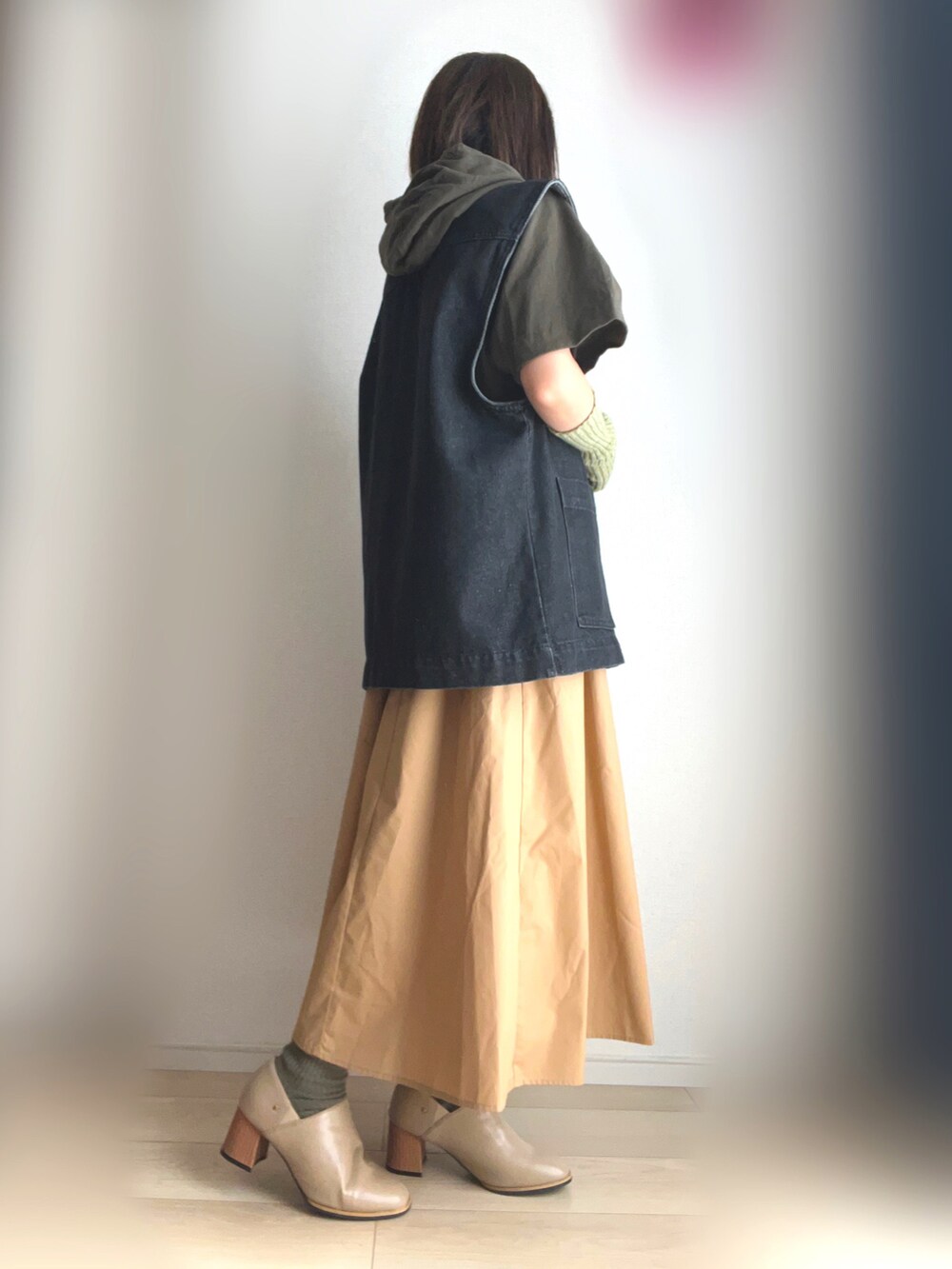 グリーン系のTシャツ/カットソー、ブラック系のベスト、ベージュ系のスカートを着用したレディースの秋コーディネートの2枚目の写真