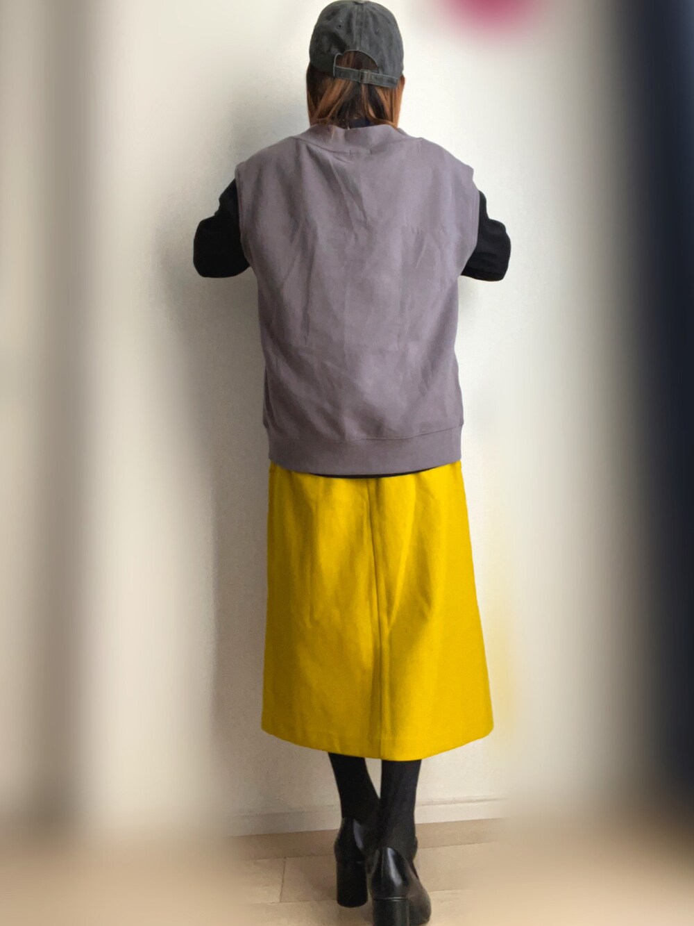 グレー系のベスト、イエロー系のスカート、ブラック系のパンプスを着用したレディースの冬コーディネートの3枚目の写真