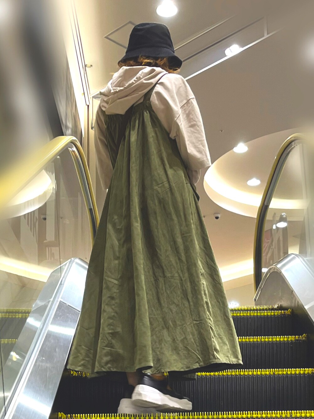 ベージュ系のパーカー、グリーン系のジャンパースカート、ブラック系のスニーカーを着用したレディースの秋コーディネートの2枚目の写真