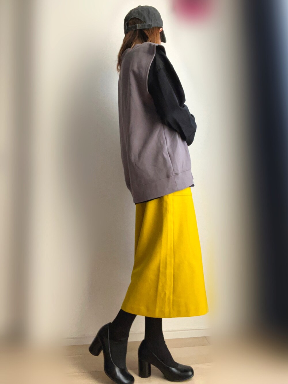 グレー系のベスト、イエロー系のスカート、ブラック系のパンプスを着用したレディースの冬コーディネートの2枚目の写真