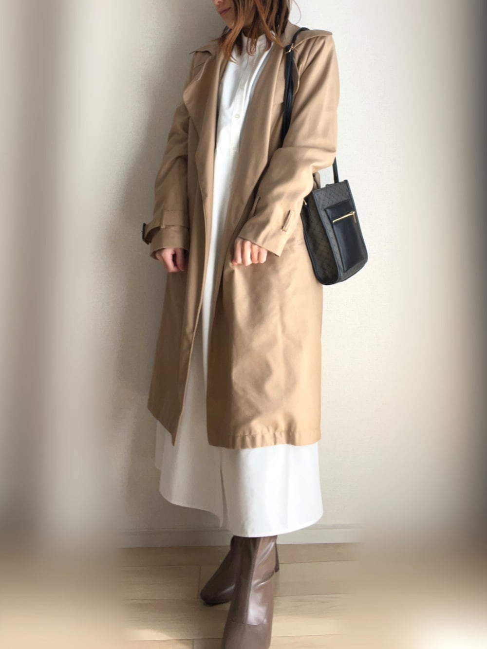 ベージュ系のトレンチコート、ホワイト系のシャツワンピース、ブラウン系のブーツを着用したレディースの冬コーディネートの2枚目の写真