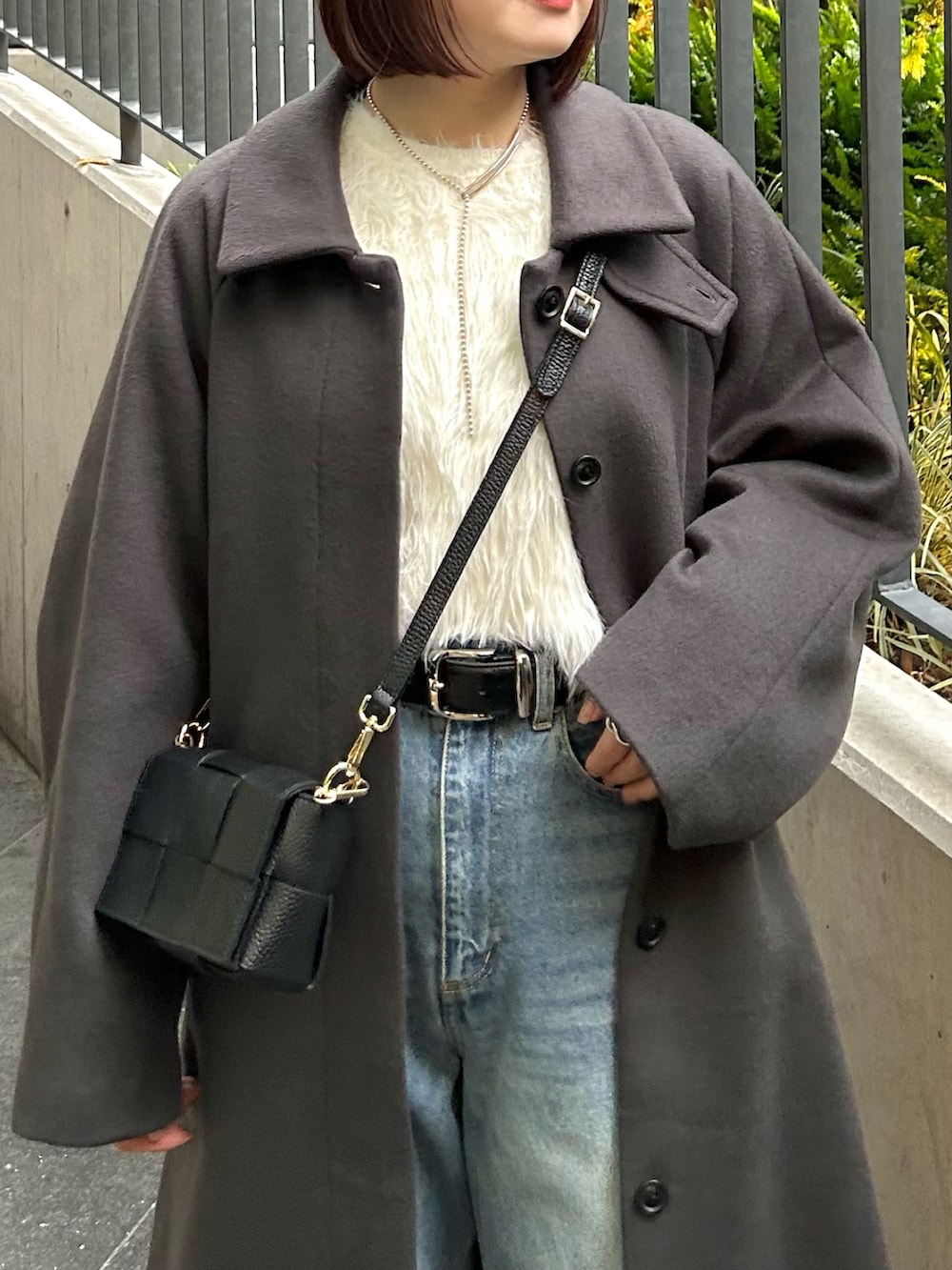 グレー系のステンカラーコート、ホワイト系のニット/セーター、ブルー系のデニムパンツを着用したレディースの秋コーディネートの3枚目の写真