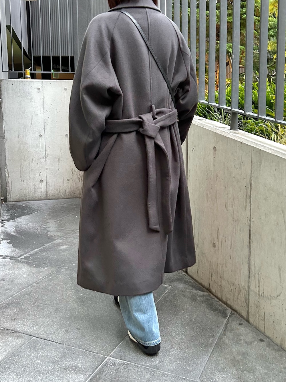 グレー系のステンカラーコート、ホワイト系のニット/セーター、ブルー系のデニムパンツを着用したレディースの秋コーディネートの4枚目の写真