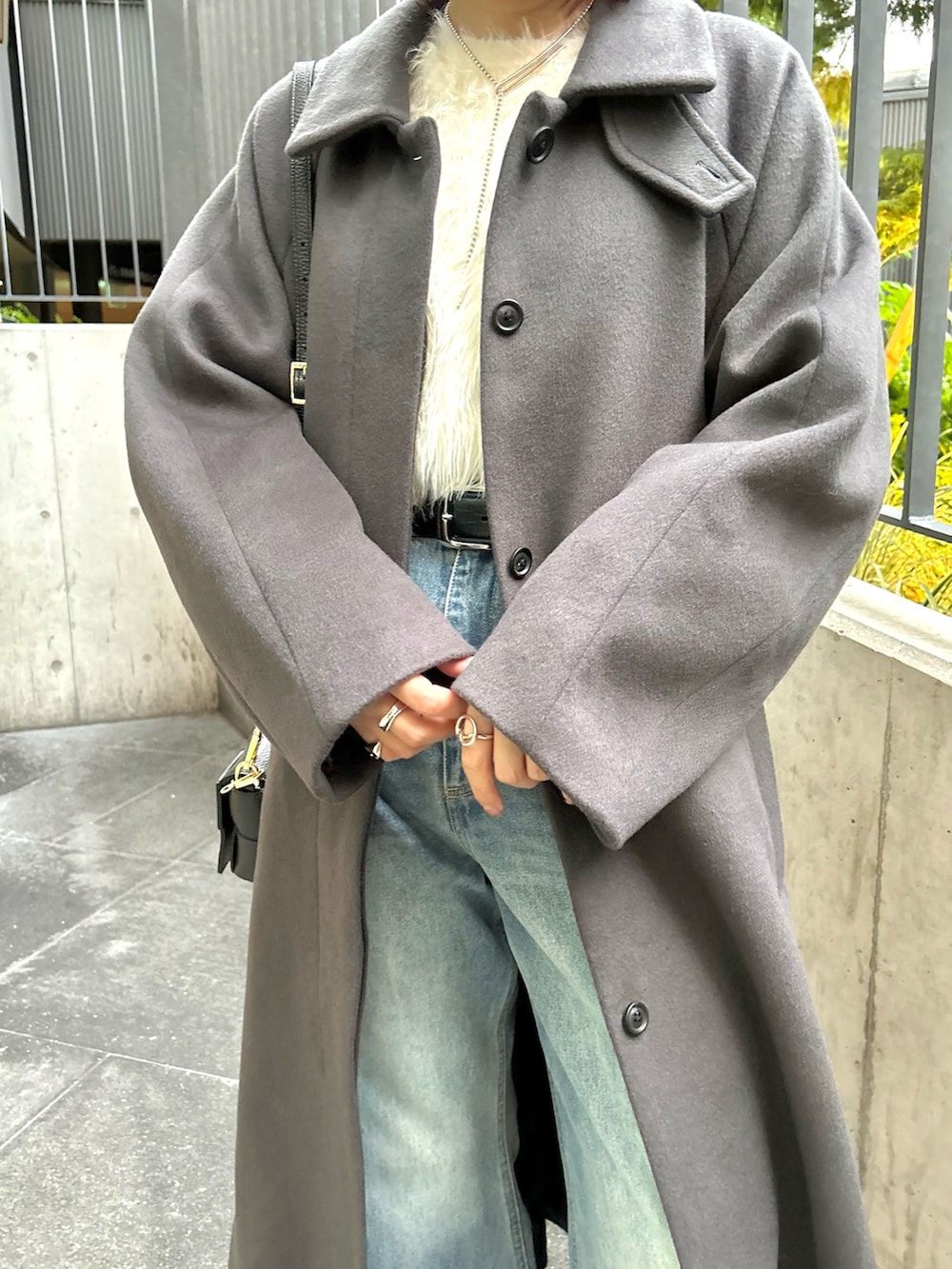 グレー系のステンカラーコート、ホワイト系のニット/セーター、ブルー系のデニムパンツを着用したレディースの秋コーディネートの5枚目の写真