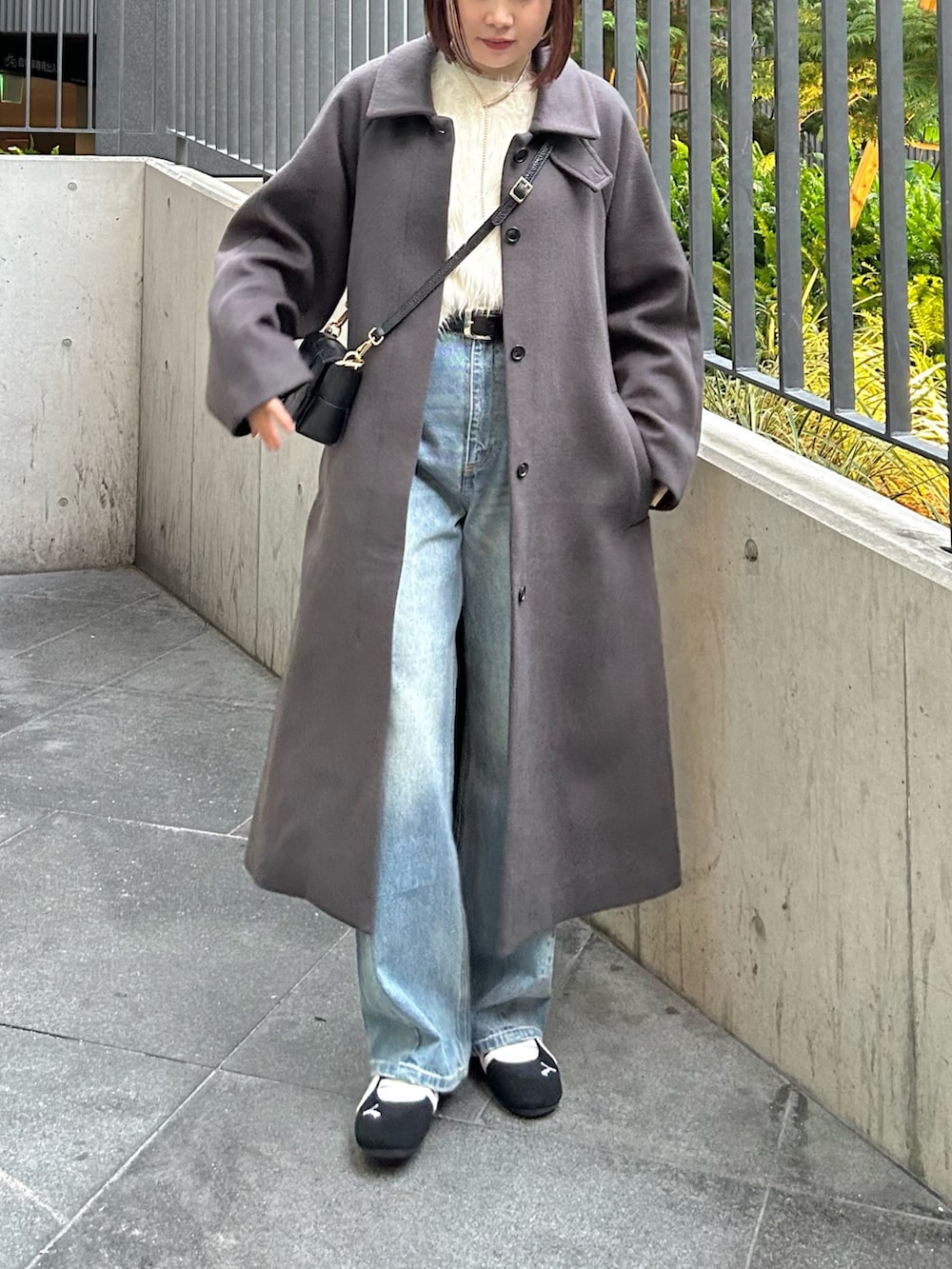 グレー系のステンカラーコート、ホワイト系のニット/セーター、ブルー系のデニムパンツを着用したレディースの秋コーディネートの2枚目の写真
