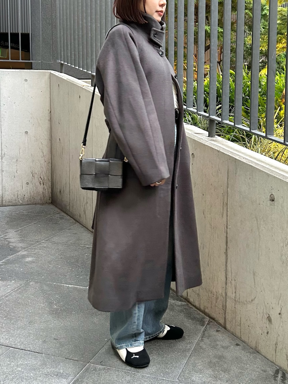 グレー系のステンカラーコート、ホワイト系のニット/セーター、ブルー系のデニムパンツを着用したレディースの秋コーディネートの6枚目の写真