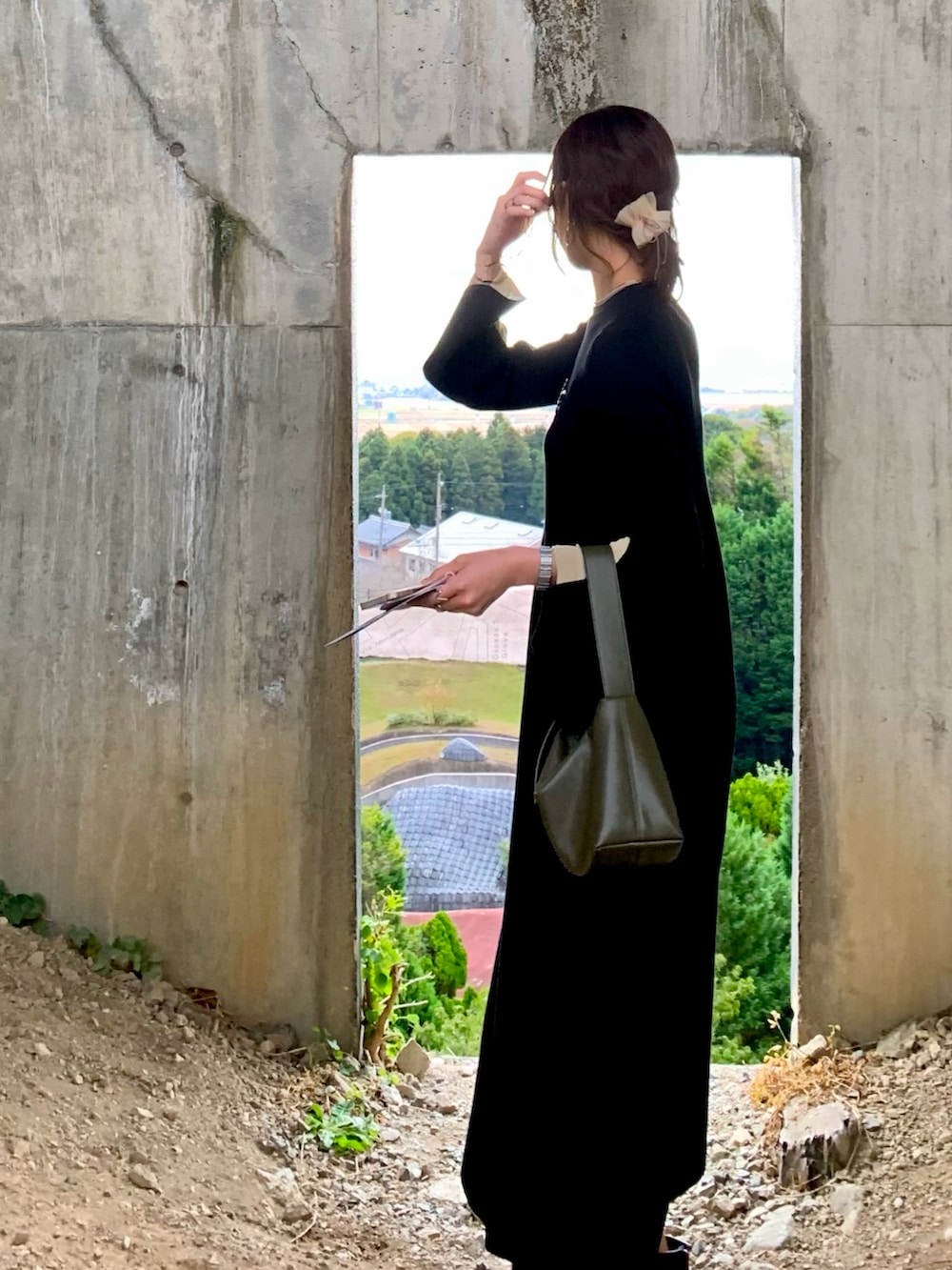 ブラック系のワンピース、グリーン系のハンドバッグ、ブラウン系のブーツを着用したレディースの秋コーディネートの2枚目の写真