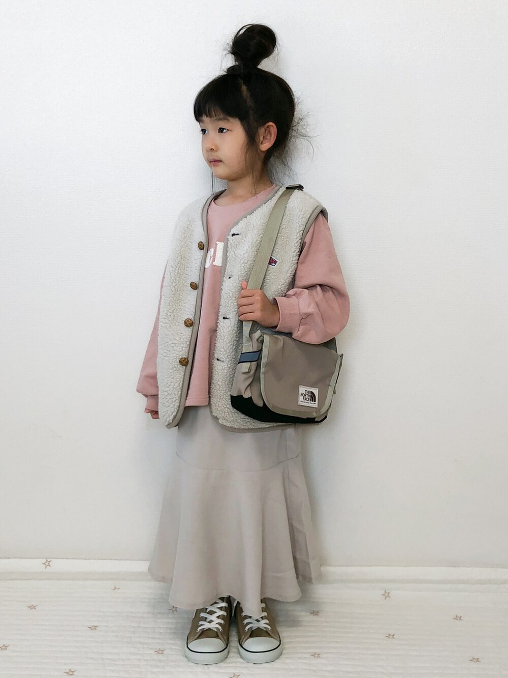 ホワイト系のベスト、ベージュ系のスニーカー、ベージュ系のショルダーバッグを着用したキッズの冬コーディネートの3枚目の写真