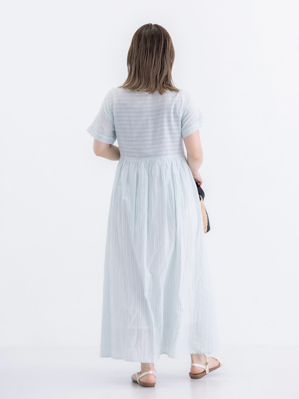 ベージュ系のかごバッグ、ゴールド系のサンダル、グリーン系のワンピースを着用したレディースの夏コーディネートの3枚目の写真