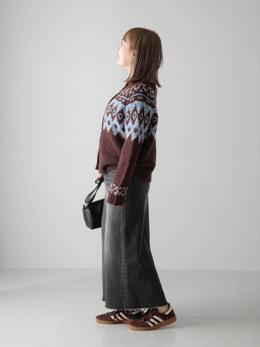 ブラック系のショルダーバッグ、ブラウン系のカーディガン/ボレロ、ブラック系のデニムスカートを着用したレディースの秋コーディネートの2枚目の写真