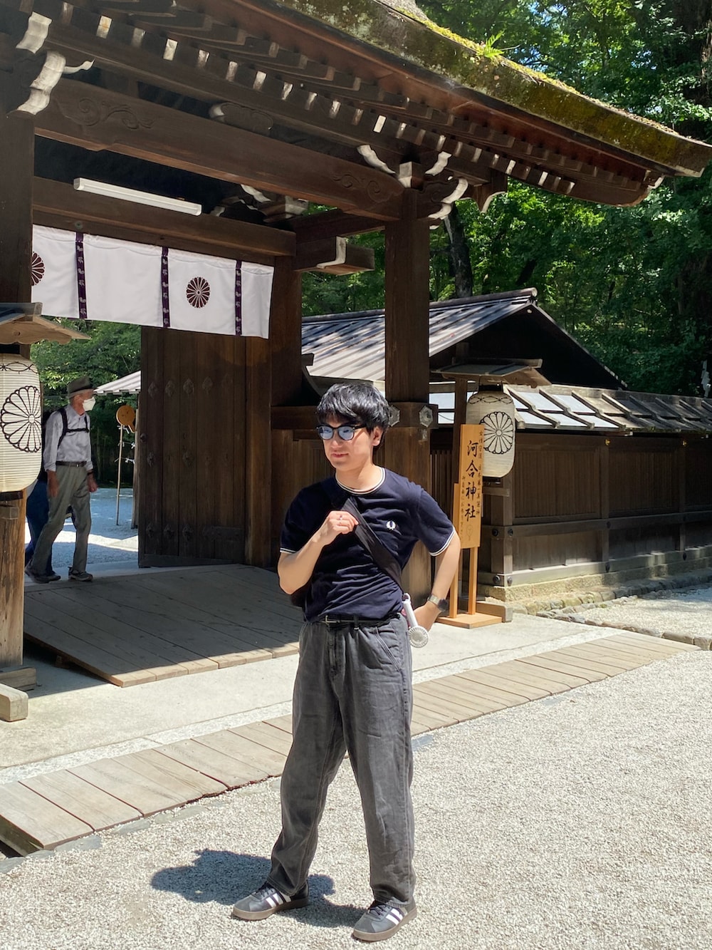 ブラック系のスニーカー、ブラック系のデニムパンツ、ホワイト系のショルダーバッグを着用したメンズの秋コーディネートの2枚目の写真