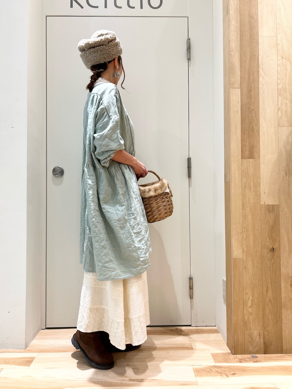 グリーン系のチュニック、ホワイト系のスカート、ブラウン系のブーツを着用したレディースの冬コーディネートの2枚目の写真