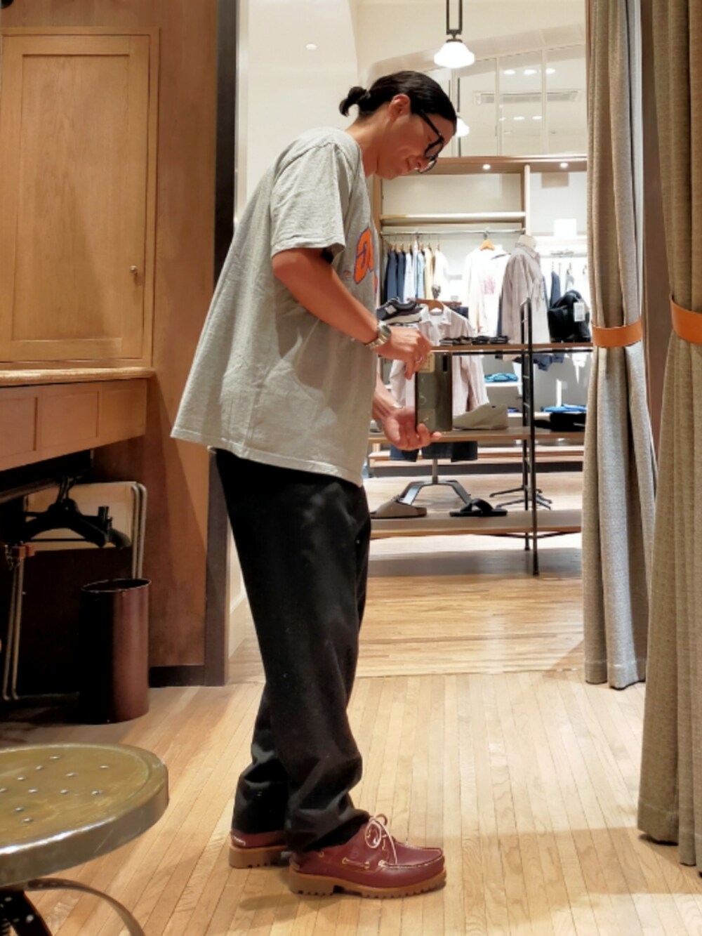 グレー系のTシャツ/カットソー、ブラック系のスラックス、ブラウン系のモカシン/デッキシューズを着用したメンズの夏コーディネートの2枚目の写真