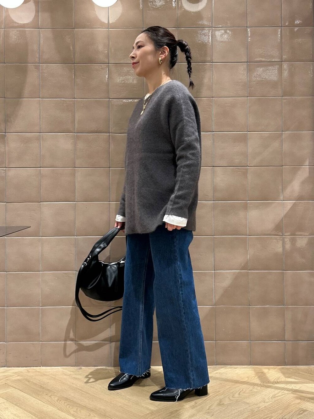 グレー系のニット/セーター、ブルー系のデニムパンツ、ブラック系のハンドバッグを着用したレディースの秋コーディネートの2枚目の写真