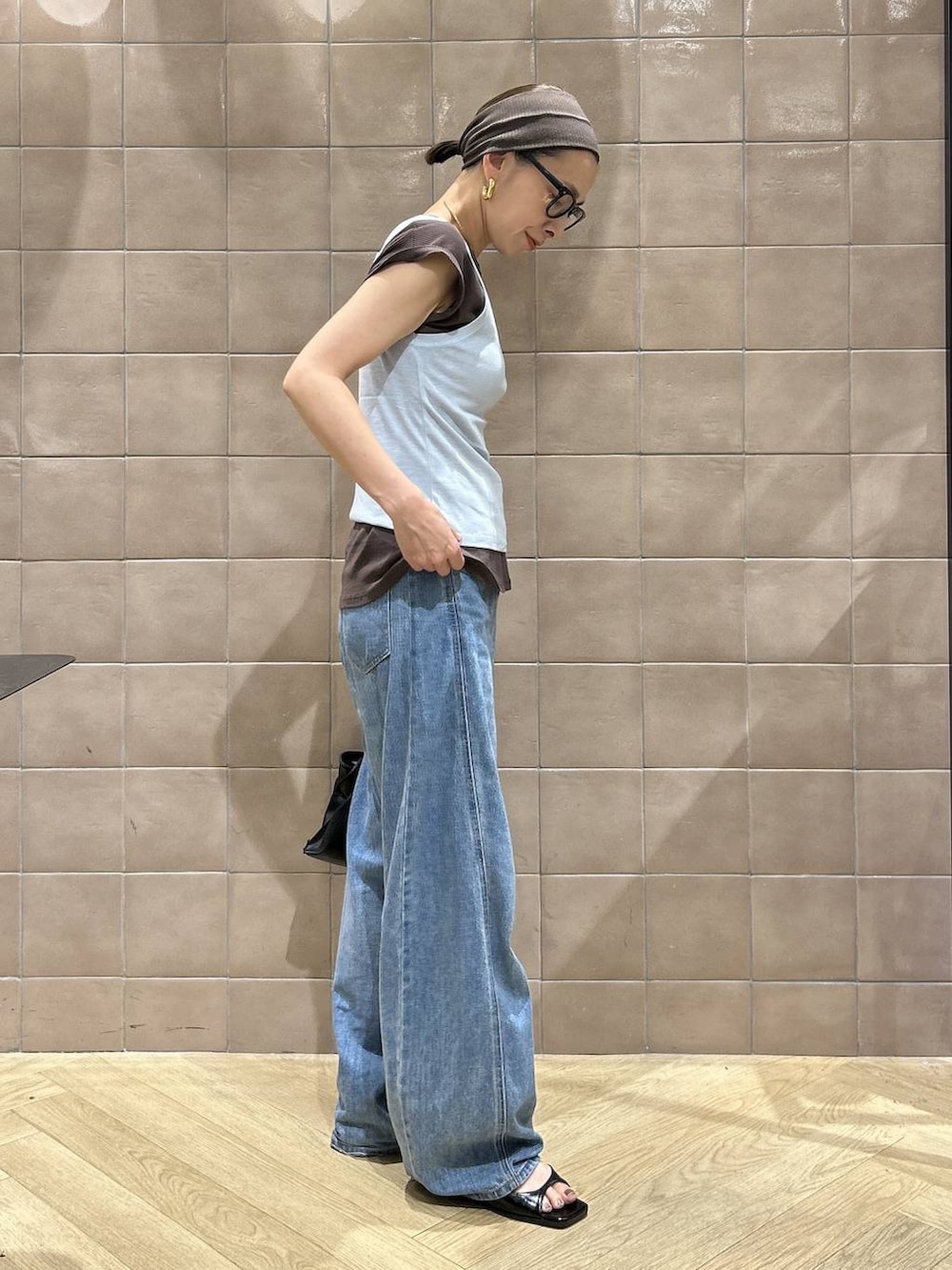 ブラック系のショルダーバッグ、ブラウン系のTシャツ/カットソー、ブルー系のデニムパンツを着用したレディースの夏コーディネートの7枚目の写真