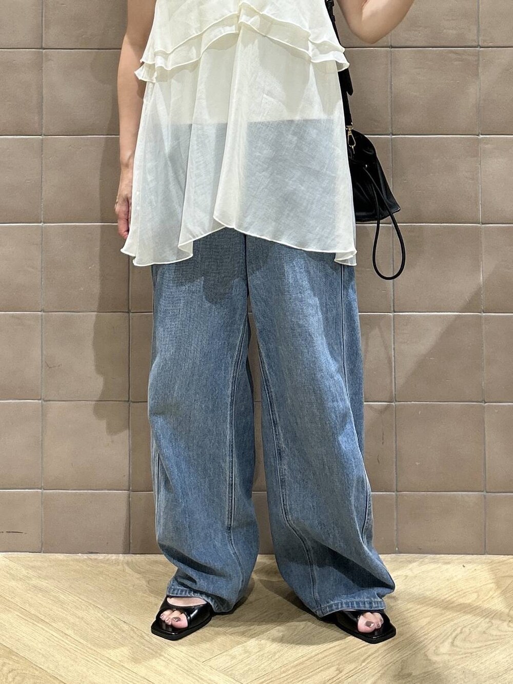 ブラック系のショルダーバッグ、ホワイト系のキャミソール、ブルー系のデニムパンツを着用したレディースの夏コーディネートの3枚目の写真