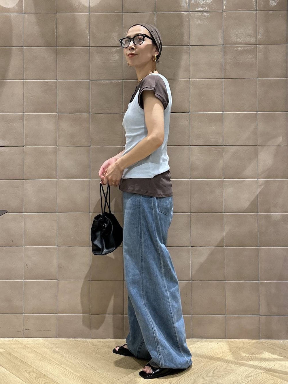 ブラック系のショルダーバッグ、ブラウン系のTシャツ/カットソー、ブルー系のデニムパンツを着用したレディースの夏コーディネートの5枚目の写真