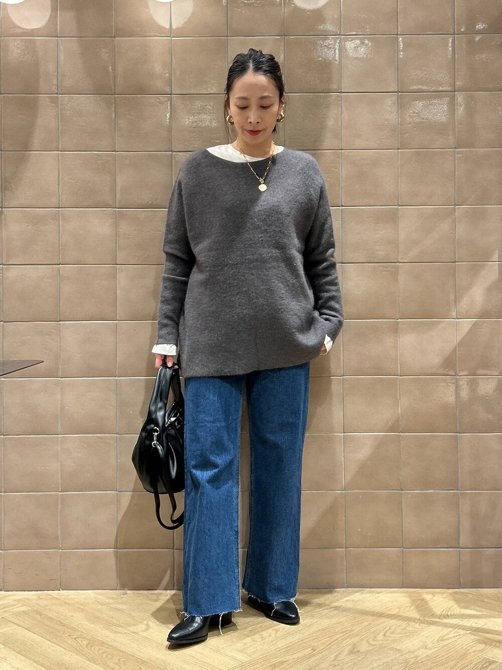 グレー系のニット/セーター、ブルー系のデニムパンツ、ブラック系のハンドバッグを着用したレディースの秋コーディネートの5枚目の写真