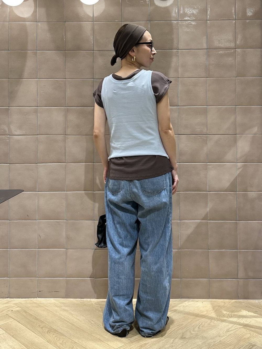 ブラック系のショルダーバッグ、ブラウン系のTシャツ/カットソー、ブルー系のデニムパンツを着用したレディースの夏コーディネートの6枚目の写真